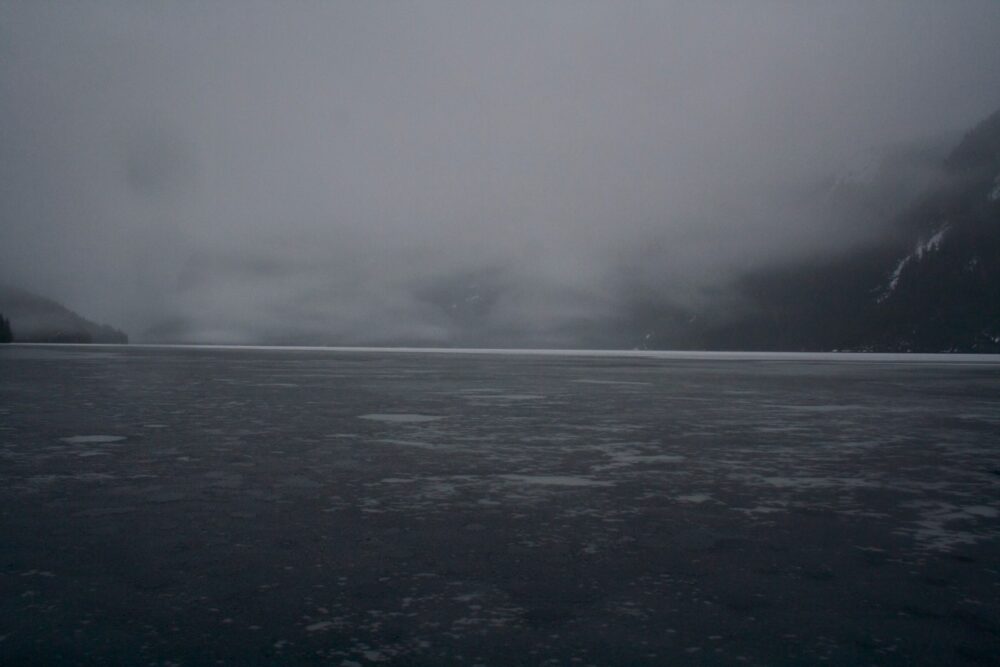 A lake covered in ice with mountains in the background.