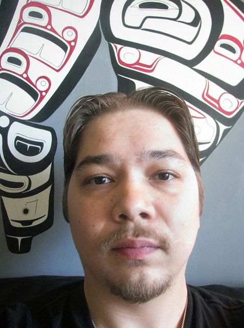 A man sitting in front of a wall with a totem pole on it.