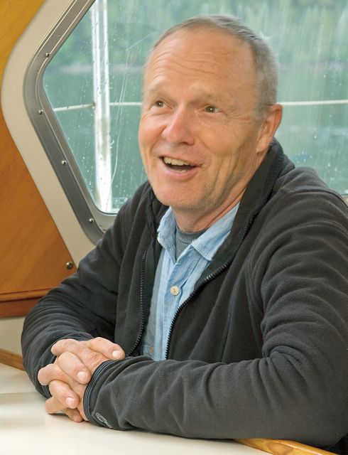 A man sits at a table on a boat with a bottle of wine.