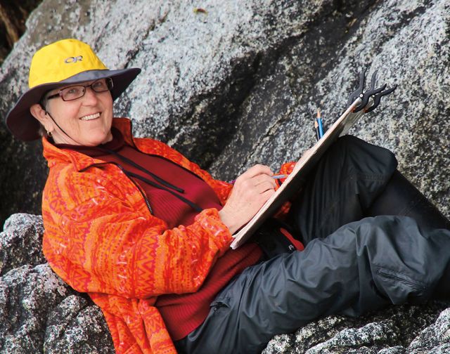 A woman wearing an orange jacket and orange hat is sitting on a rock.