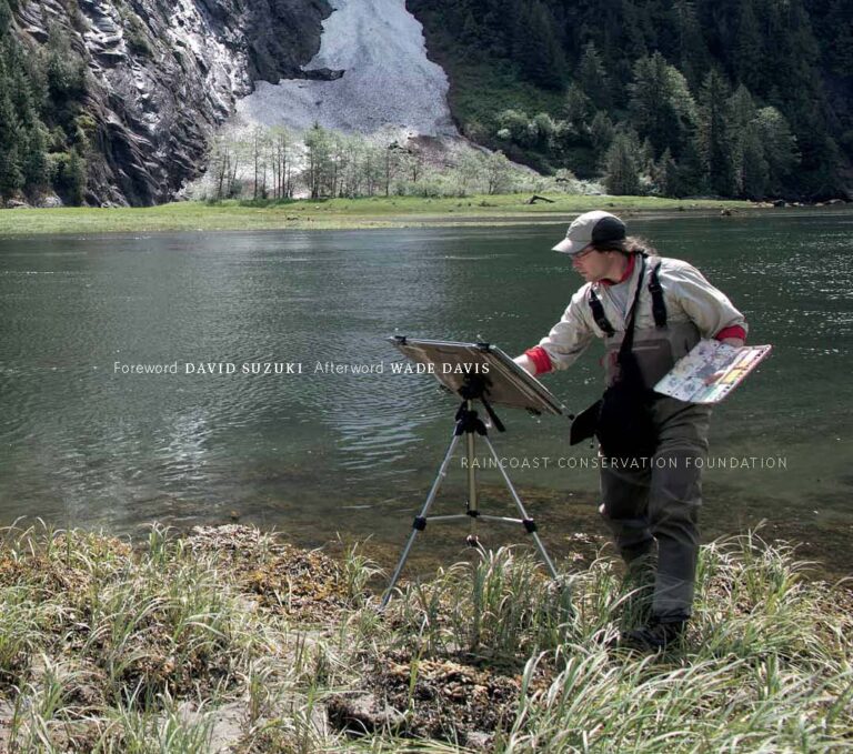A man painting in front of a lake with mountains in the background.