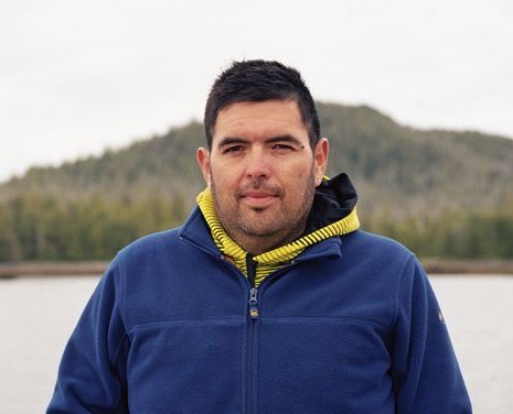 A man in a blue jacket standing in front of a body of water.