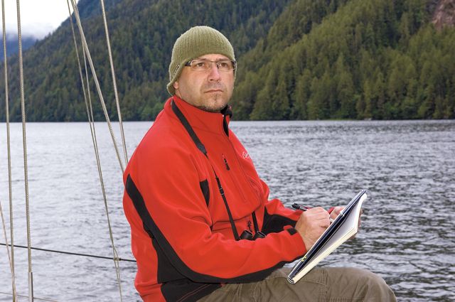 A man sitting on a sailboat holding a notebook.