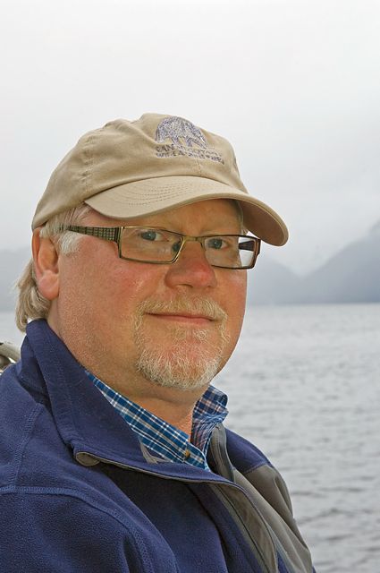 A man wearing a hat and a jacket standing by a body of water.