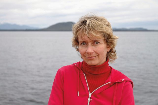 A woman in a red sweater standing near a body of water.