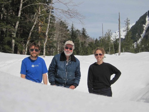 Three people standing in the snow with a mountain in the background.