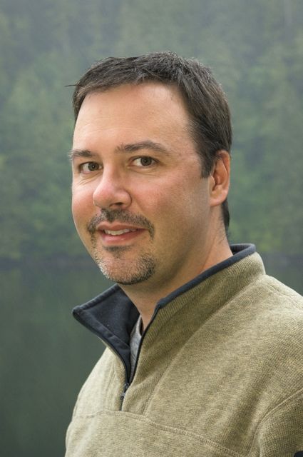 A man in a sweater standing in front of a lake.