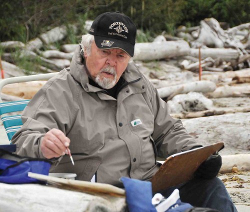 An older man sitting on a beach with a clipboard.