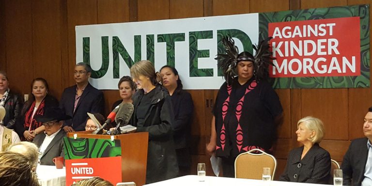 A group of people standing in front of a banner that says united against kinder morgan.