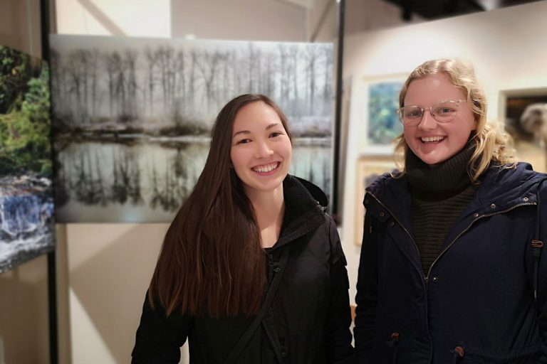 Two women stand in front of the One Shot for Coastal Carnivores exhibit at the Robert Bateman Centre.