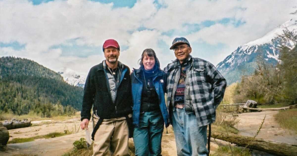 Three people standing in front of beautiful mountainous scenery.