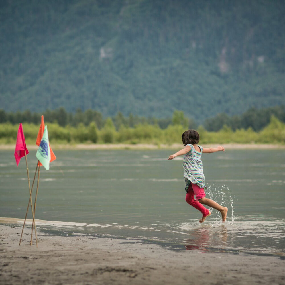 A young person jumps and plays splashing water in the Fraser River.
