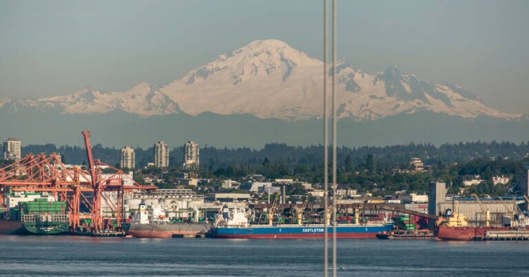 A view of the mountains over Vancouver, a layer of smog in the mid ground, and ships at rest in the foreground of the Salish Sea.
