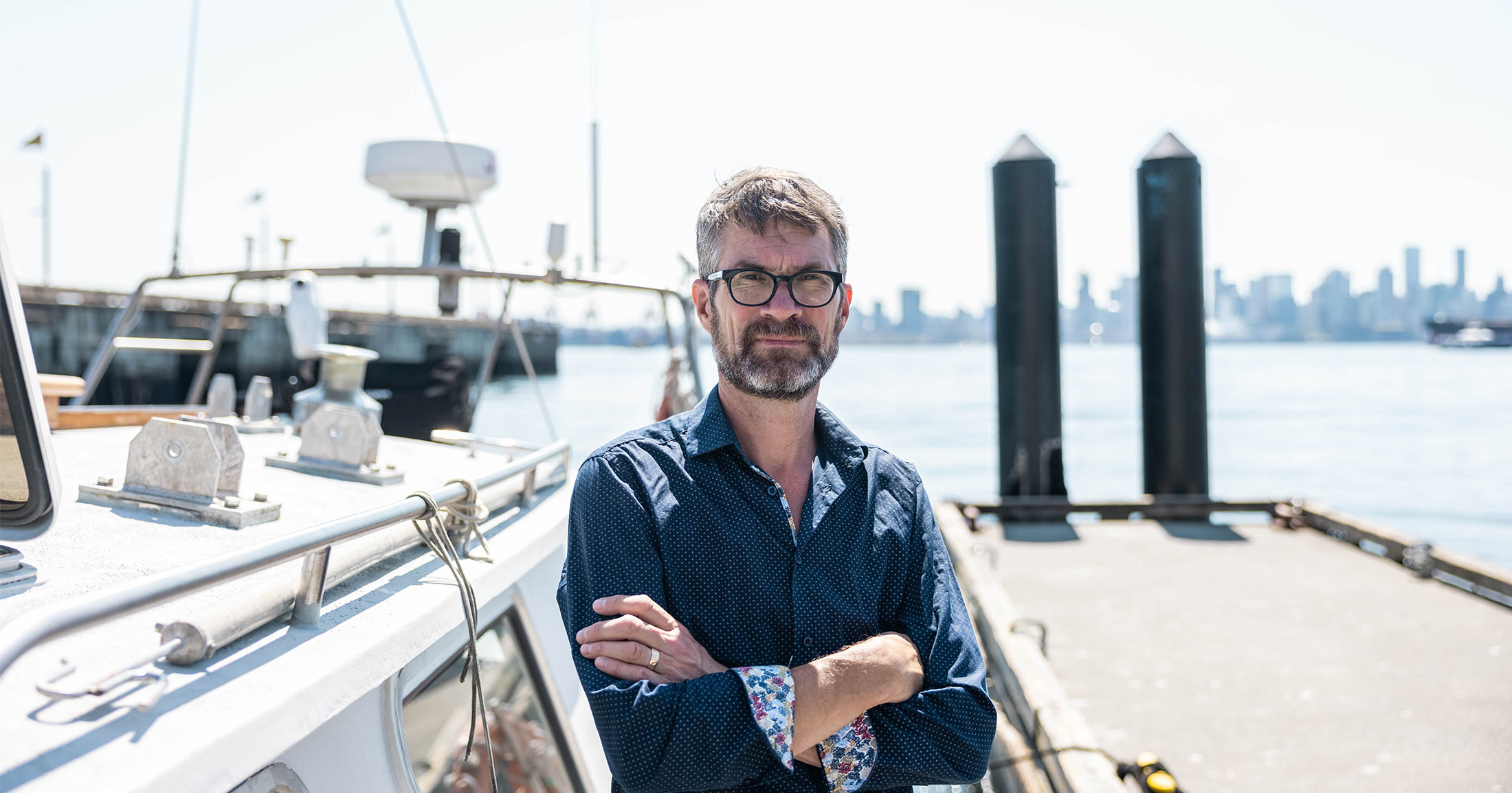 Peter Ross standing with his arms crossed with the ocean behind them.