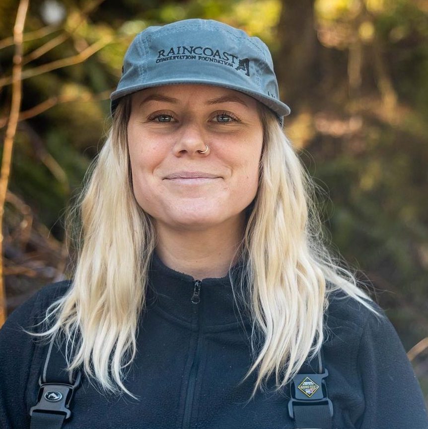 Chelsea Greer, Wolf Conservation Program Coordinator, with her Raincoast hat and rain gear, smiling into the forest.
