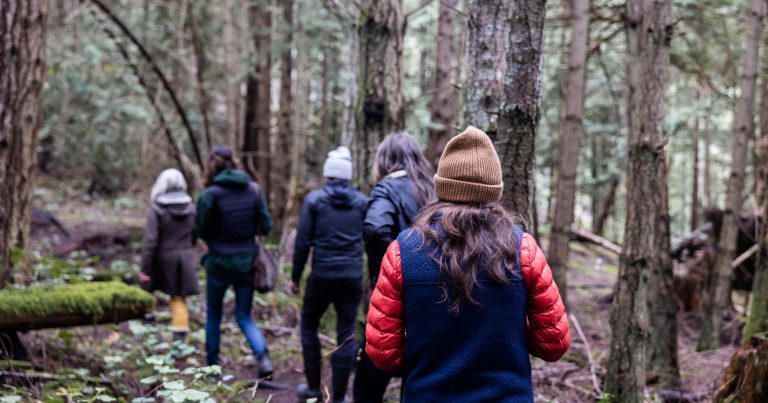 A group of conservationists and researchers and citizens walk along a path in the forest together on a tour on a cool day.