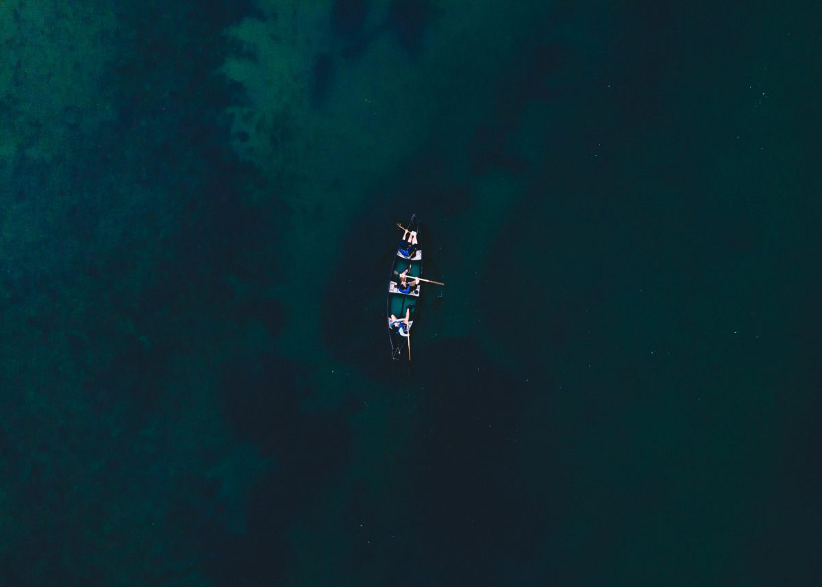 Canoe in a river with three people in it from a birds eye view. 