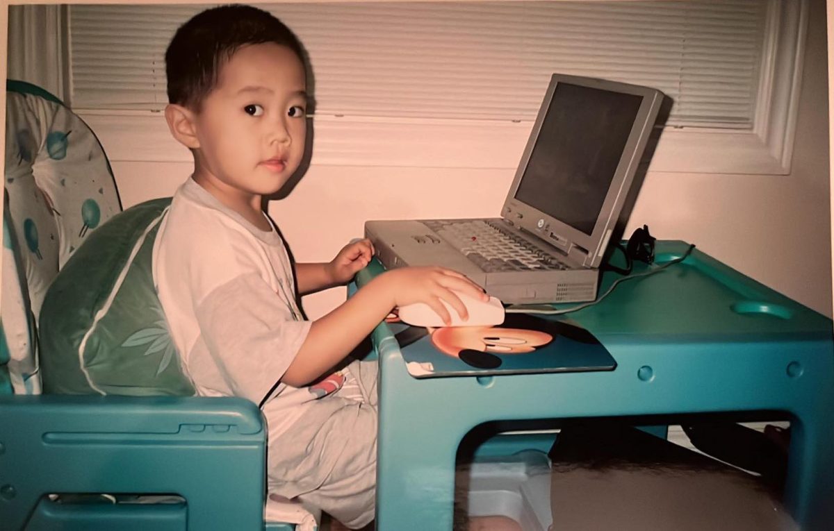 Young Auston Chhor sitting at a mini table on a very old laptop.