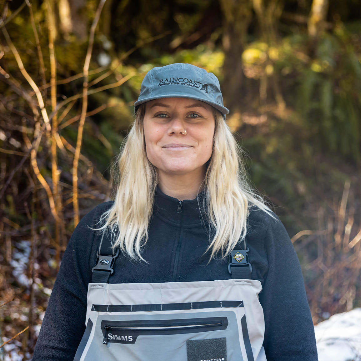 Chelsea Greer, Wolf Conservation Program Coordinator, with her Raincoast hat and rain gear, smiling into the forest.