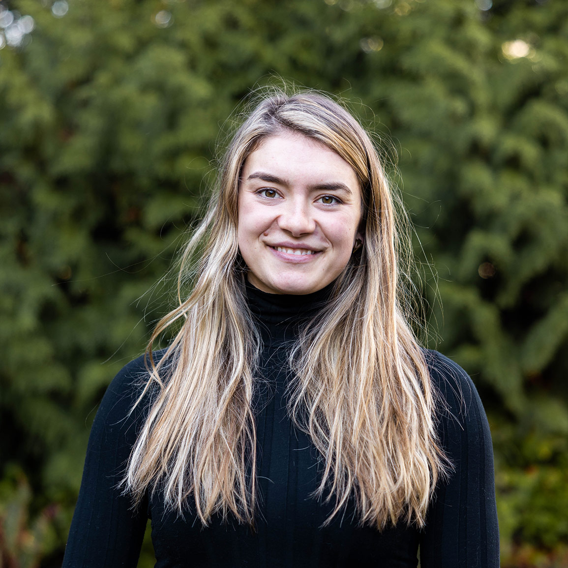 Raincoast Fellow and Masters of Science student Chenoa Shine looking at the camera, with long, straight blonde hair, wearing a black turtleneck and a green flannel jacket.