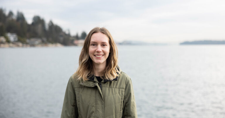 Brooke Gerle wearing a green coat smiling and standing in front of the ocean.