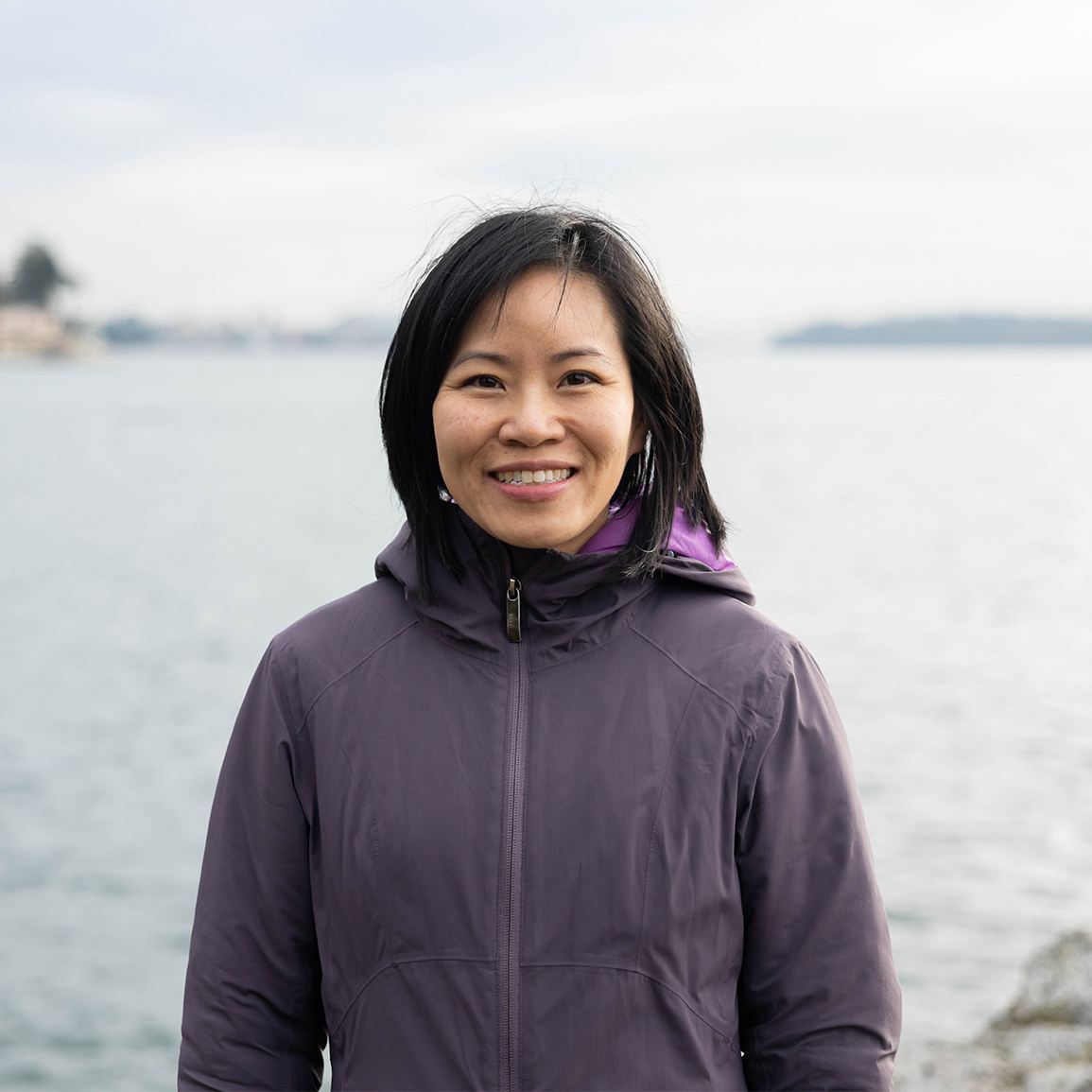 Maureen standing in front of the ocean wearing a purple jacket. 