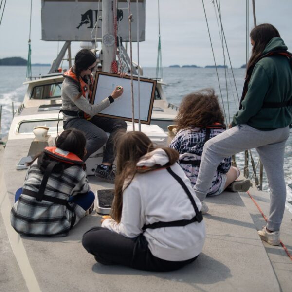 4 youth watch as someone draws on a whiteboard onboard Achiever.