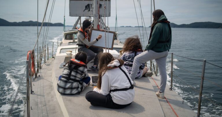 4 youth watch as someone draws on a whiteboard onboard Achiever.