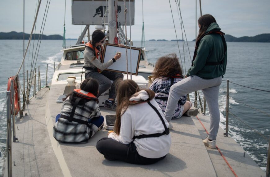 4 youth watch as someone draws on a whiteboard onboard Achiever.