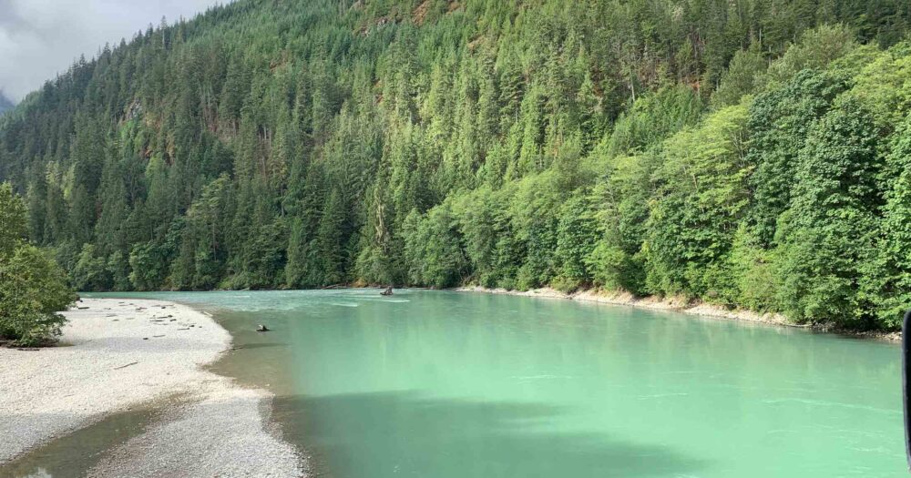 A turquoise river runs along a forested mountain.