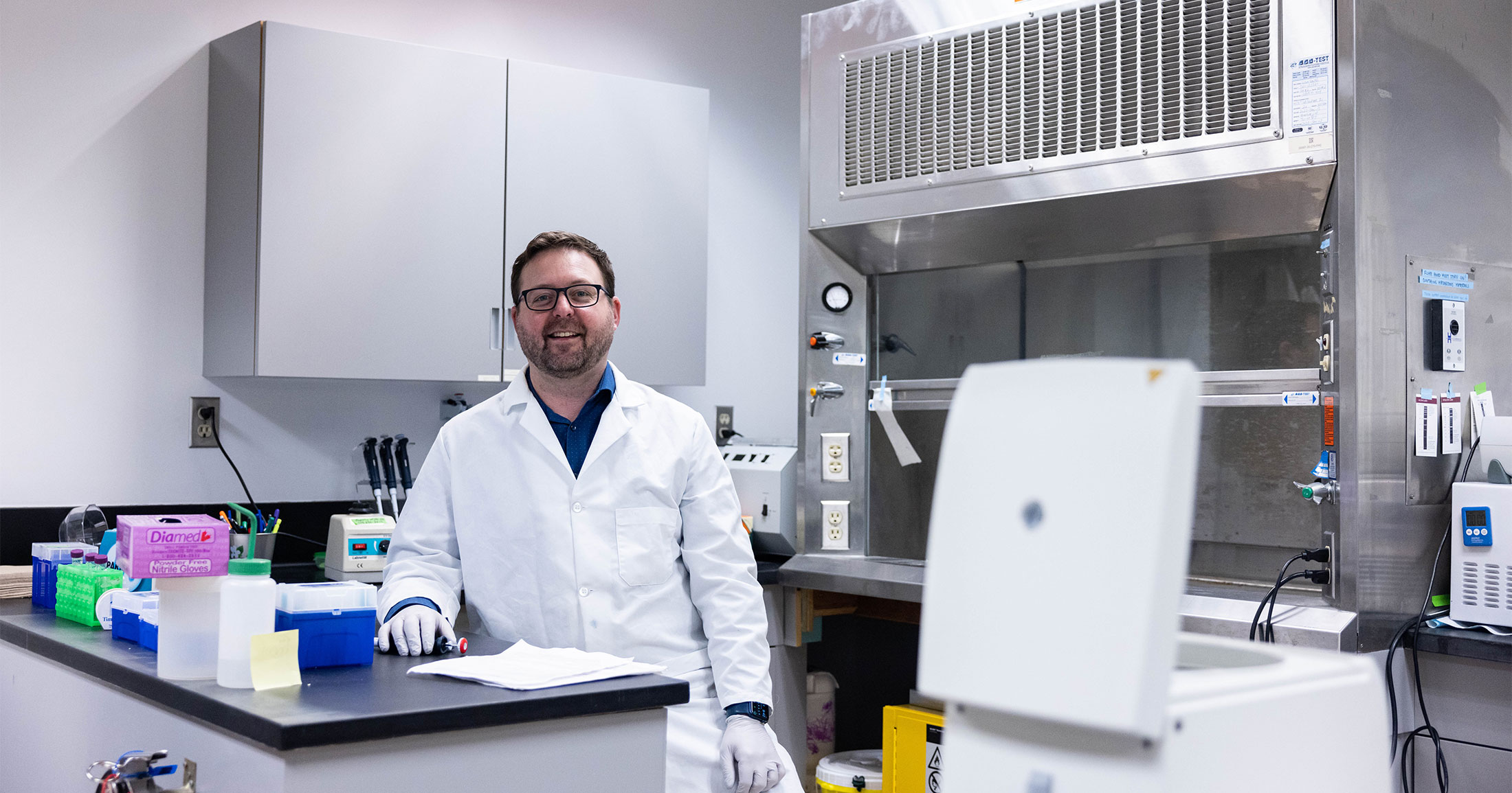 Adam Warner wearing a lab coat sitting in a lab.