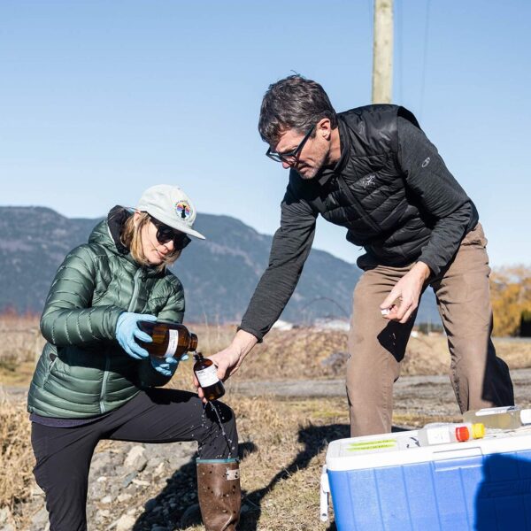 Two people working together to collect water samples in a farm field with the mountains in the background.