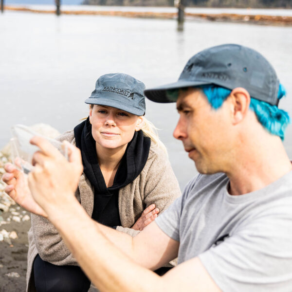 Dave Scott and Chelsea Greer looking at a salmon viewfinder while wearing Raincoast hats.