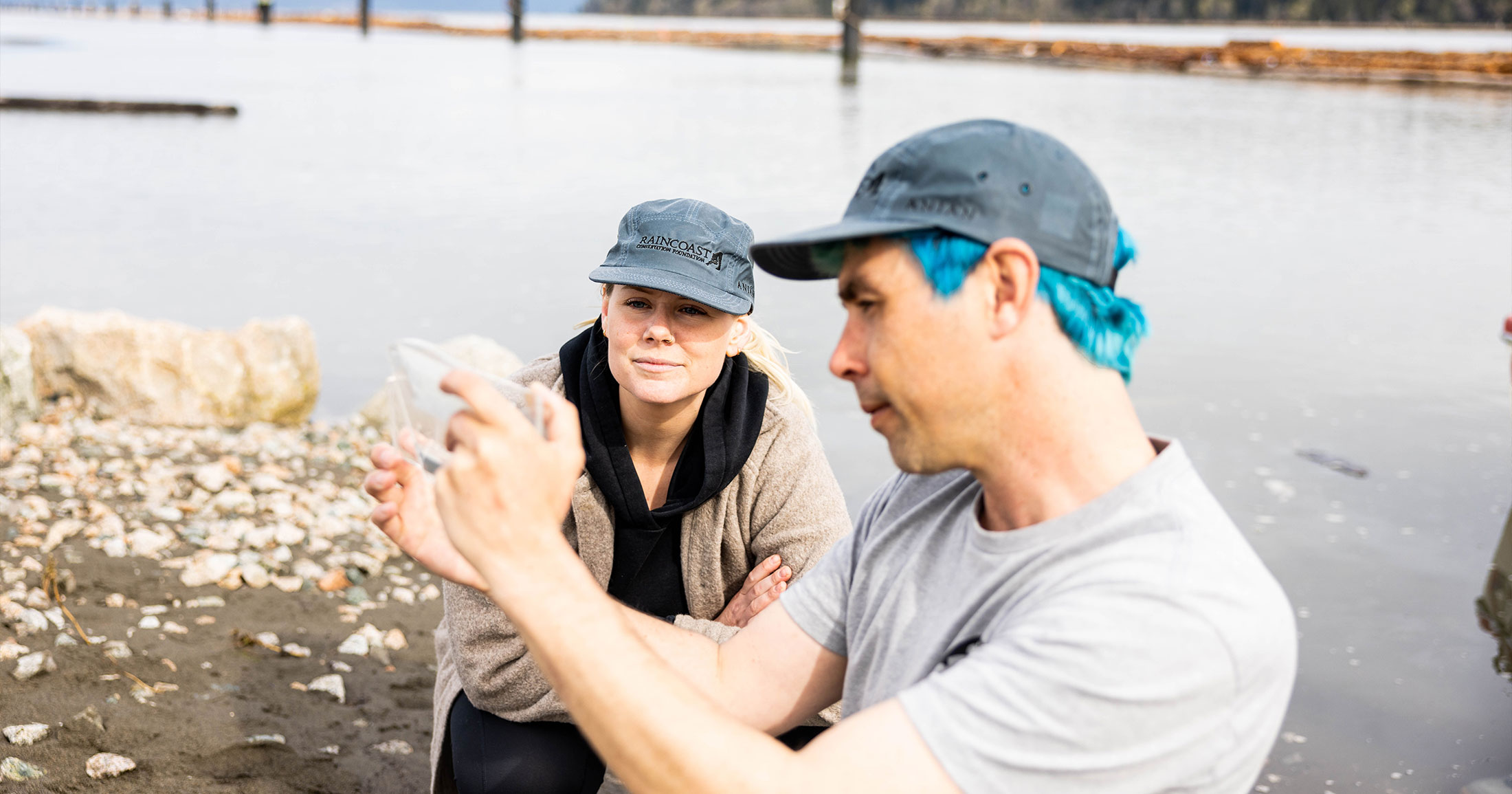 Dave Scott and Chelsea Greer looking at a salmon viewfinder while wearing Raincoast hats.