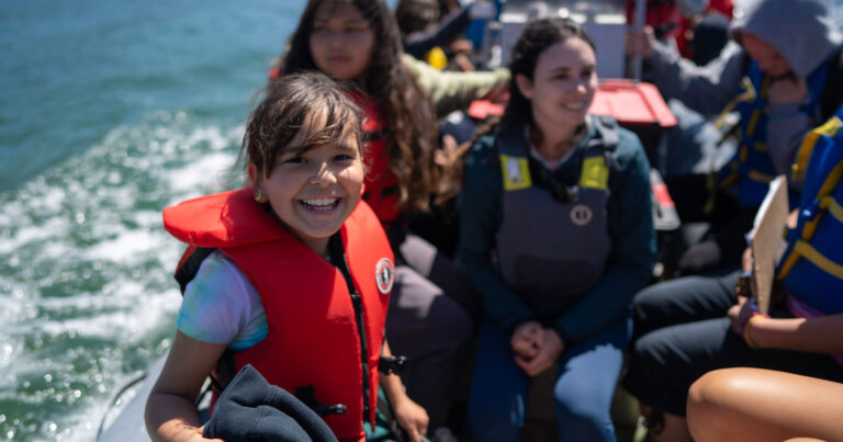 Youth on a zodiac wearing life jackets and smiling.