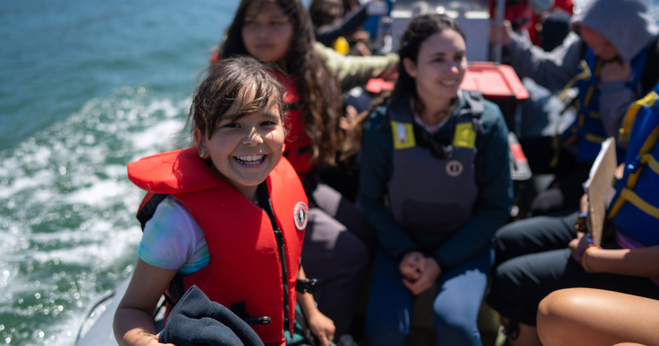 Youth on a zodiac wearing life jackets and smiling.