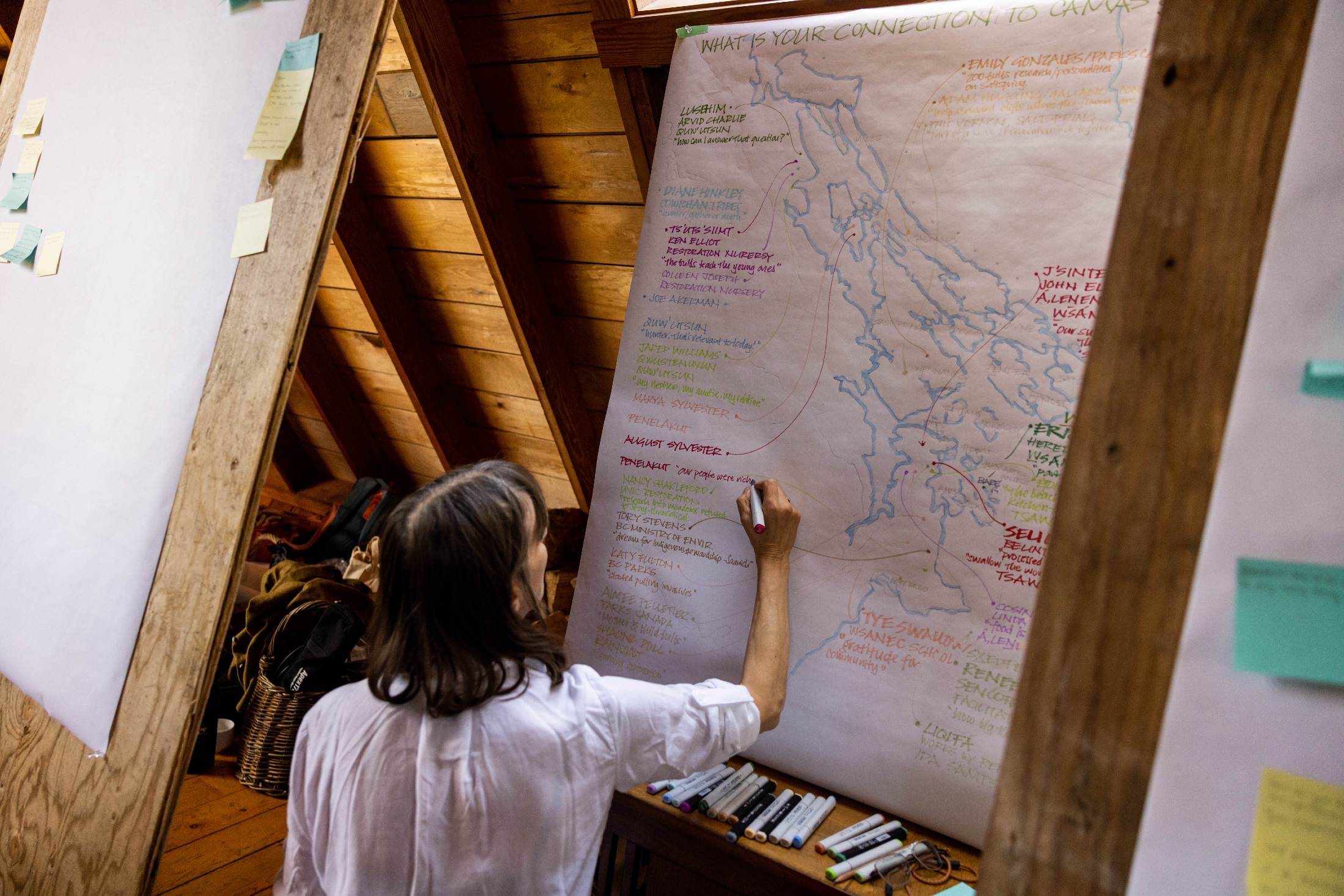 A person facing away from the camera, writing on a large piece of white paper with a hand-drawn map.
