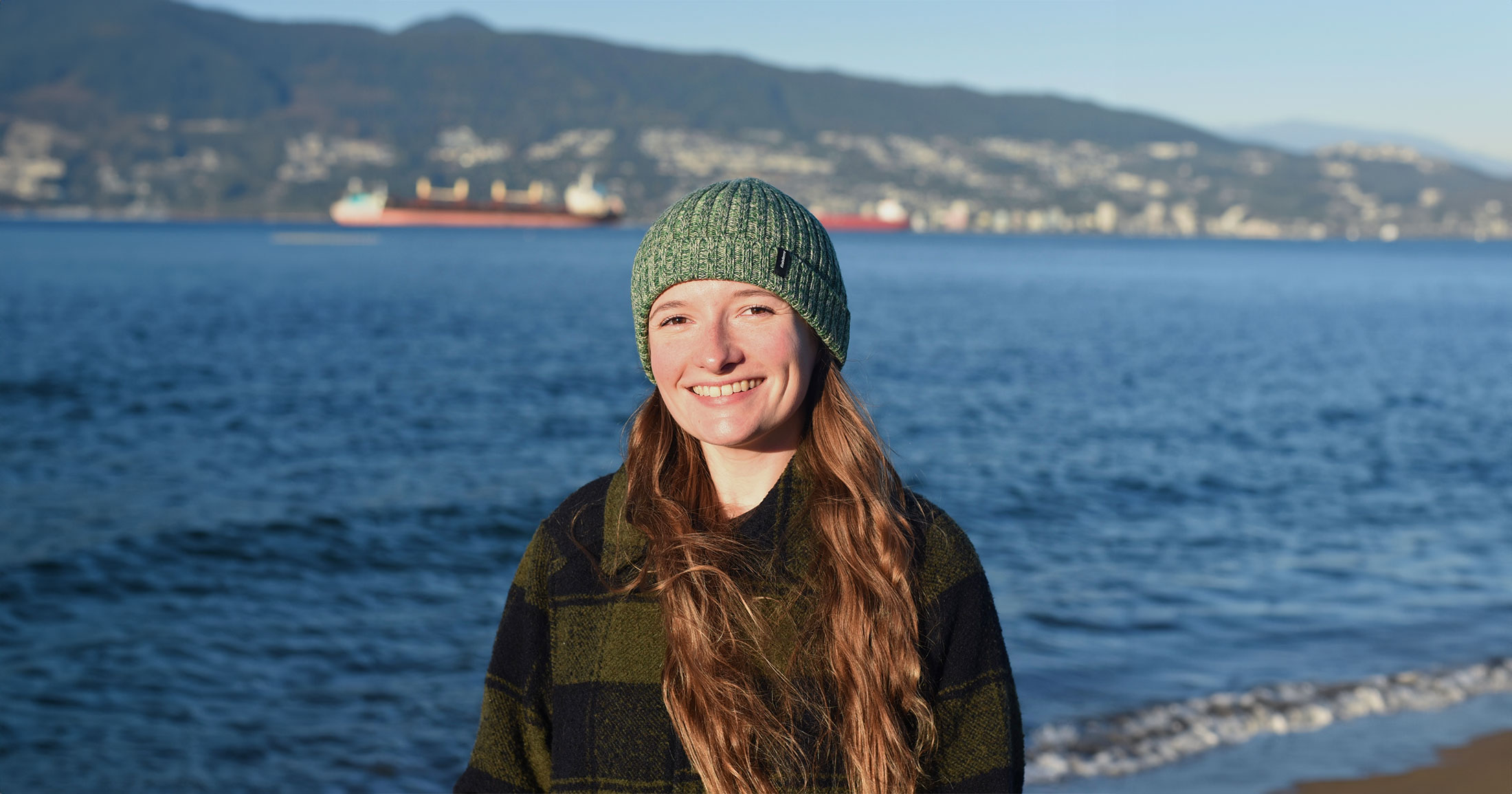 Amy Rowley, PhD, stands smiling in her toque with the Vancouver harbour in the background.