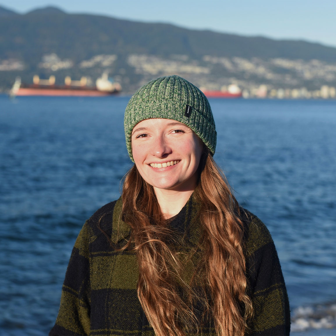 Amy Rowley, PhD, stands smiling in her toque with the Vancouver harbour in the background.