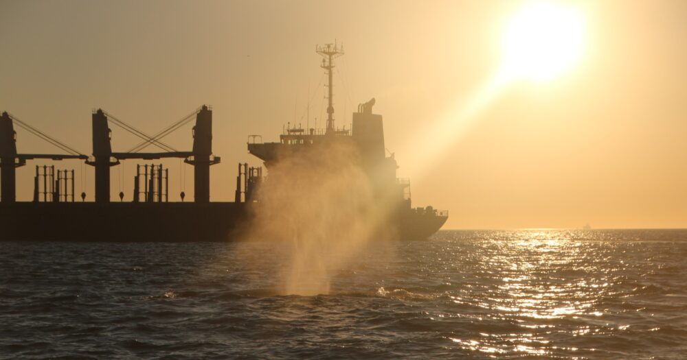 Whale blows water into the air with a large ship in the background.