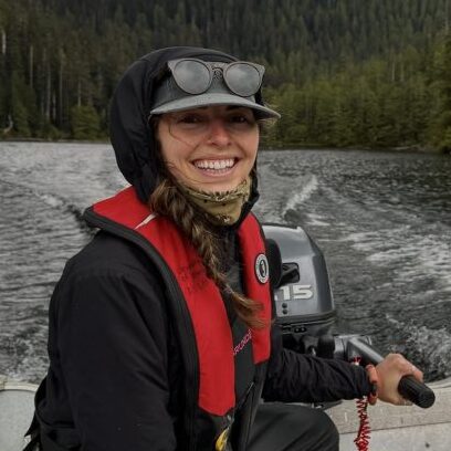 Andi Hutchinson sits at the back of a small boat wearing rain gear and a life preserver and looking very happy.