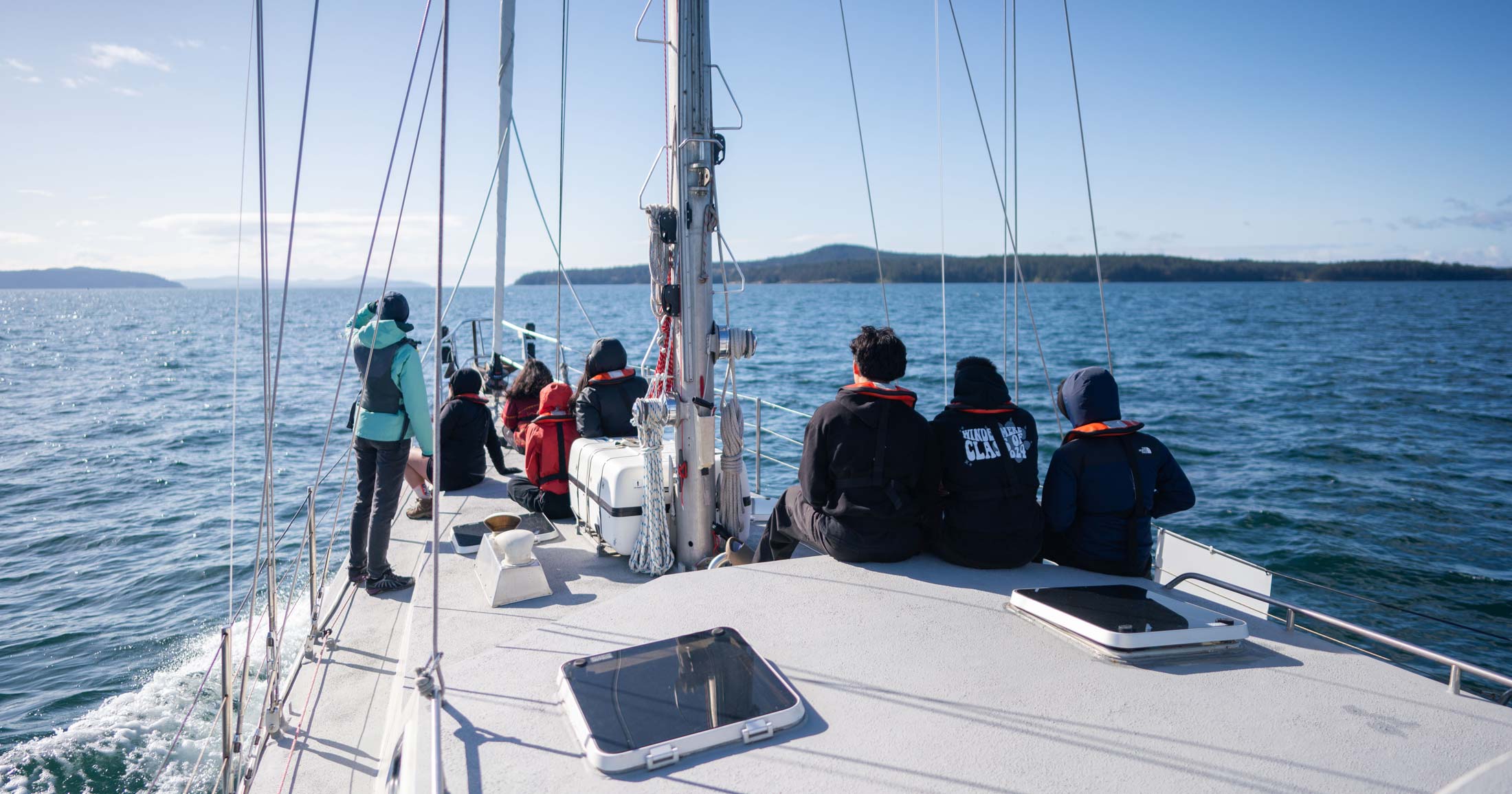 A swarm of youth sit on the bow of Achiever on a sunny day, with Pascale leading SSES curriculum.