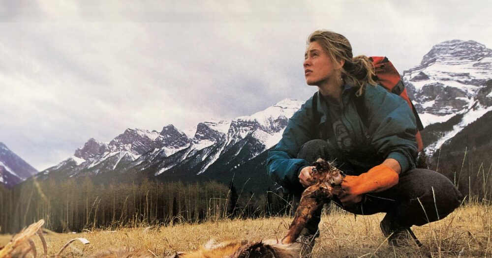 Shelley Alexander kneels over some remains in the field with stunning snow covered mountains looming in the background.