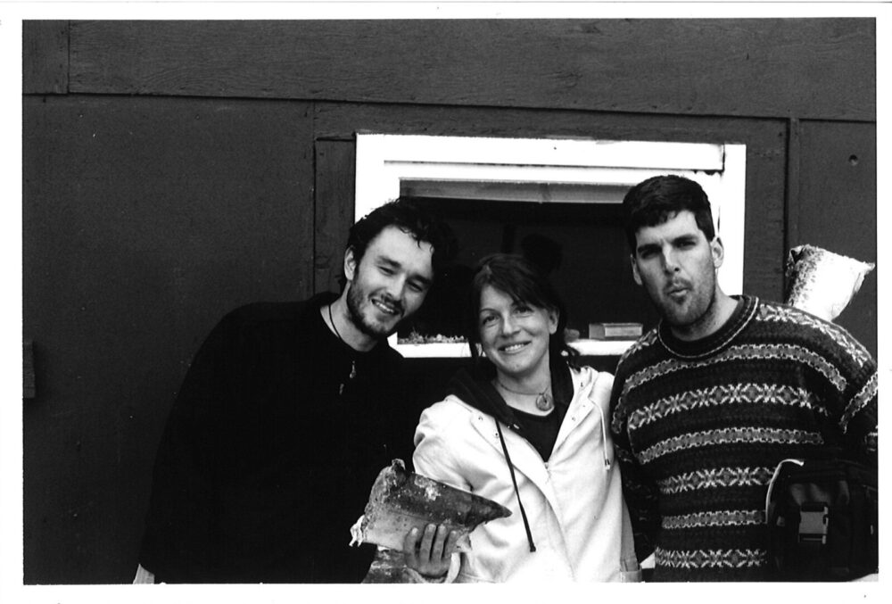 Chris, Gudrun, and Phil Clement on the deck of their field cabin, with Gudrun’s successfully halved frozen salmon, May 2002.