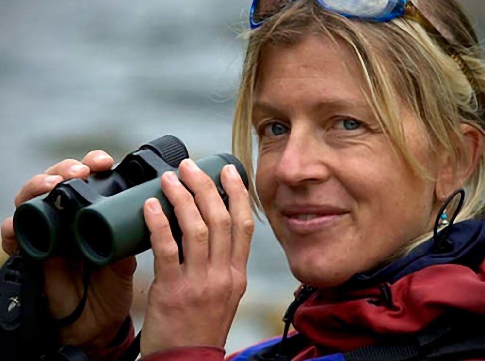 Gudrun holds her binoculars smiling.