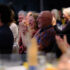 A smiling and clapping audience looks towards speaker standing out of frame.