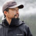 Rodney Hsu looks out over the water with mist and clouds and mountains looming behind him.