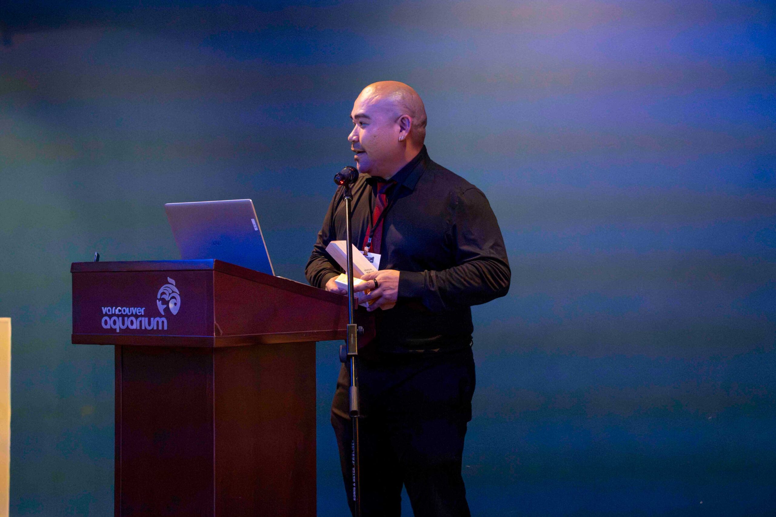 Doug Neasloss stands behind a podium speaking into a microphone accepting an award.