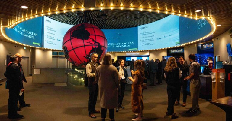 Guests stand in the entrance to the Vancouver Aquarium as the evening begins, the lights are dim as guests greet one another.