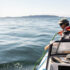 Two scientists appear on the right side of the image standing inside a small boat, placing a long wire into the ocean.